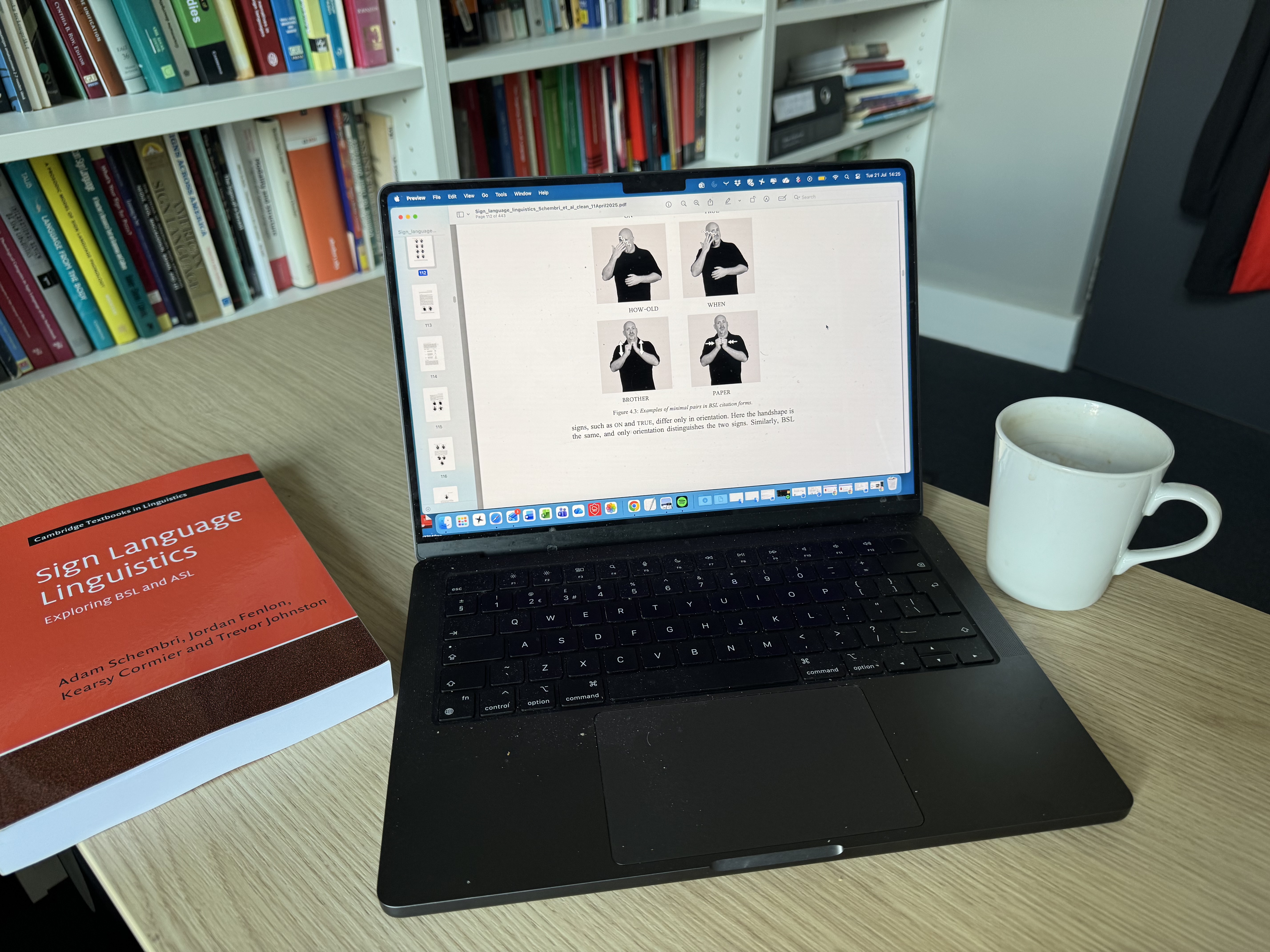 Laptop on a desk showing Sign Language Linguistics content, with the textbook and coffee mug beside it